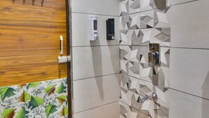 Un bagno con una porta in legno, una doccia con un motivo a piastrelle geometriche e un secchio giallo su uno sgabello blu.