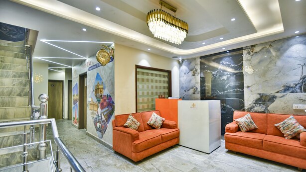 Una hall con pavimento in marmo, due divani arancioni con cuscini decorati, una reception e un grande lampadario.