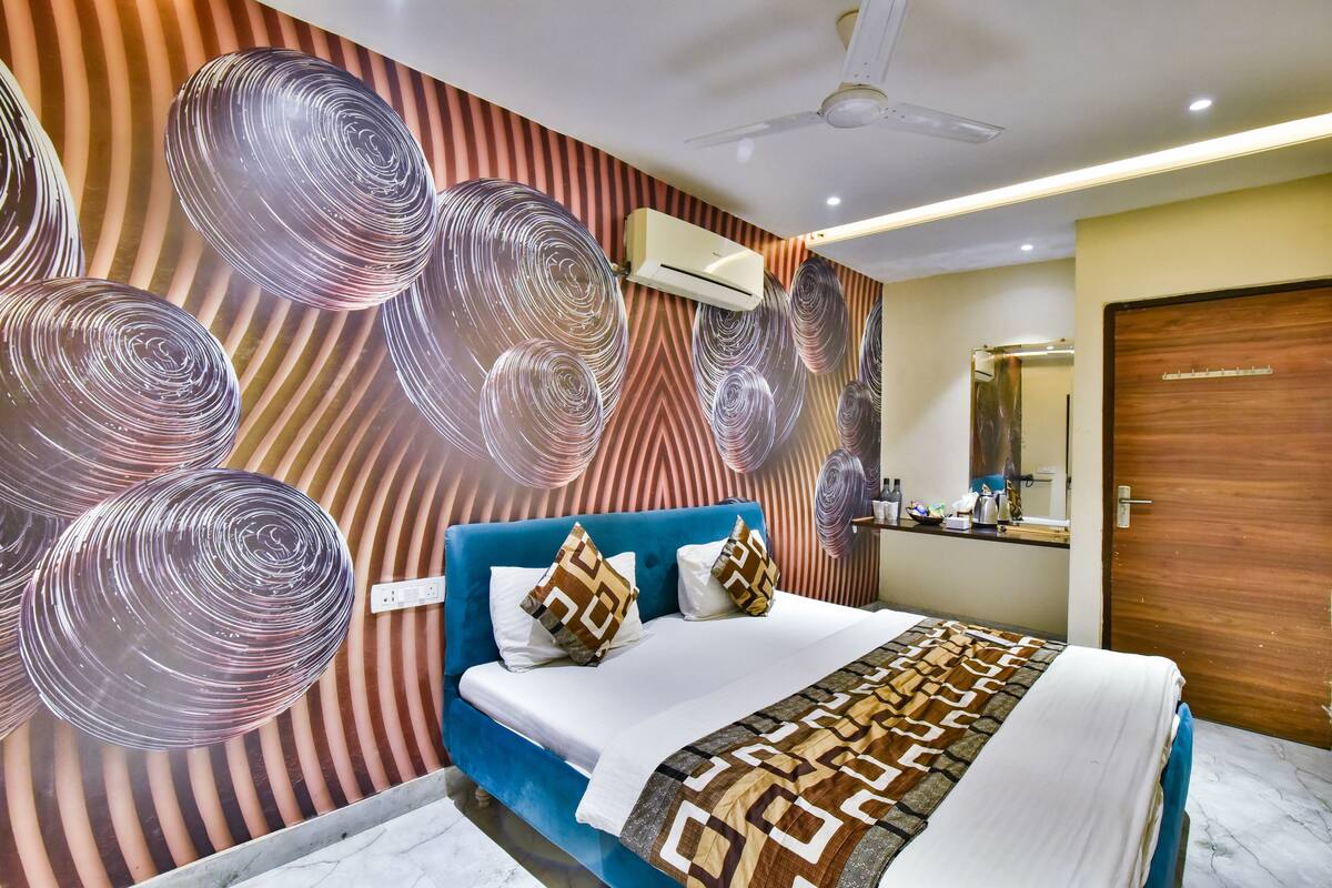 Una habitación de hotel moderna con una cama azul, decoración de pared con estampado y un ventilador de techo.