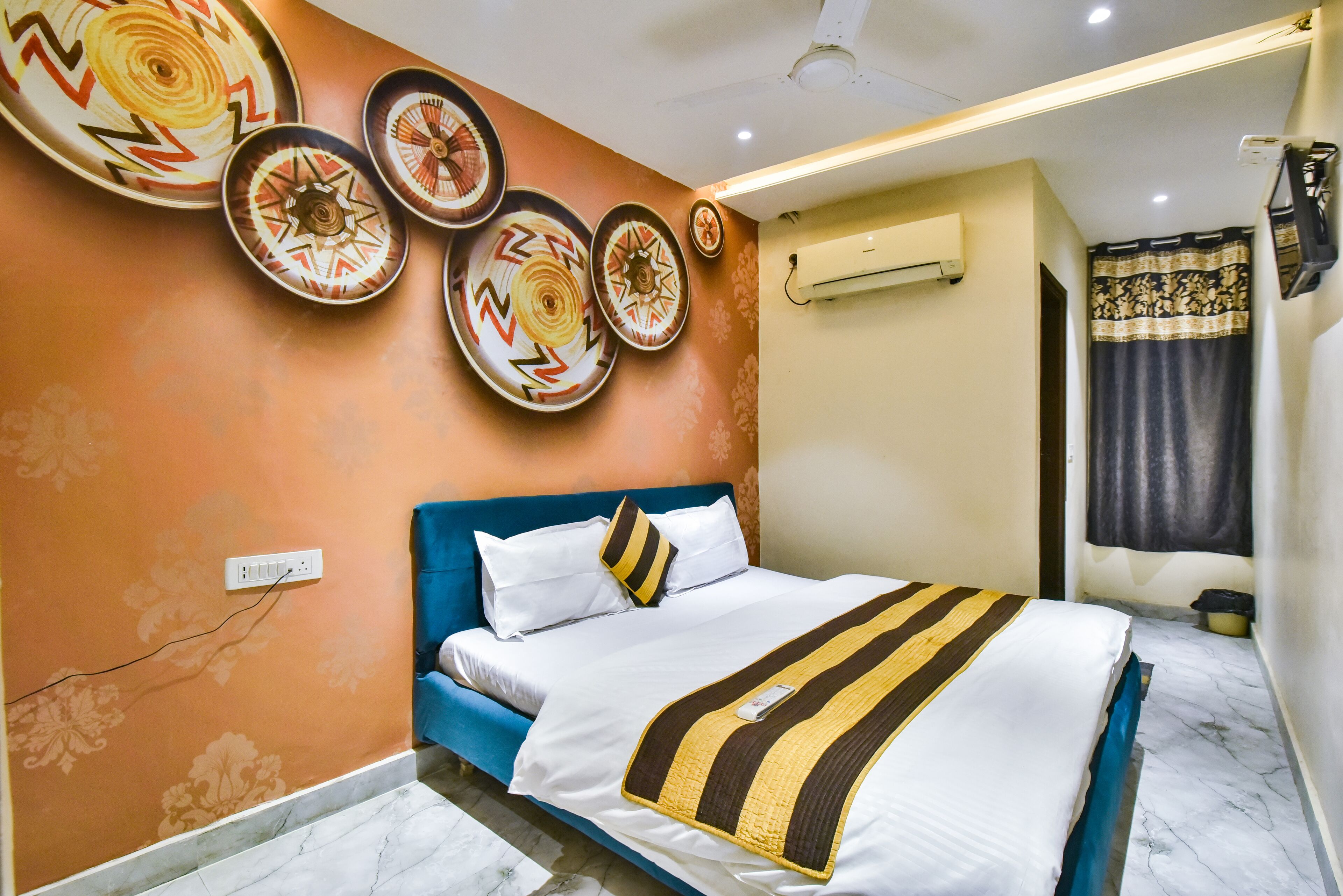 Un dormitorio con cabecera azul, cama con ropa de cama blanca y una manta a rayas, y placas decorativas en la pared, además de un equipo de aire acondicionado.