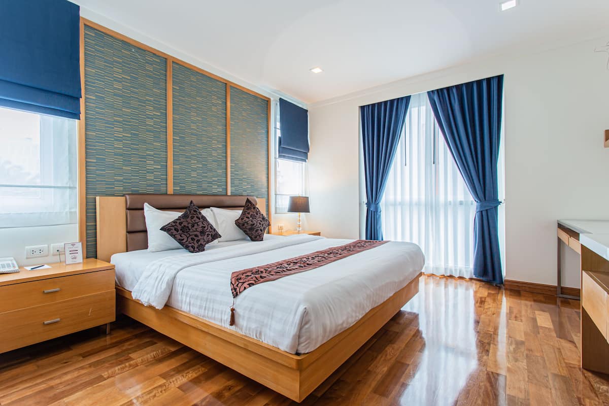A modern hotel room with a wooden bed, a nightstand, a desk, and a large window with curtains.