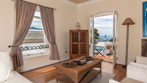 A room with a wooden table, a sofa, a cabinet, and a view of the outdoors. - Auberge Burgundy Guest House (Hermanus)
