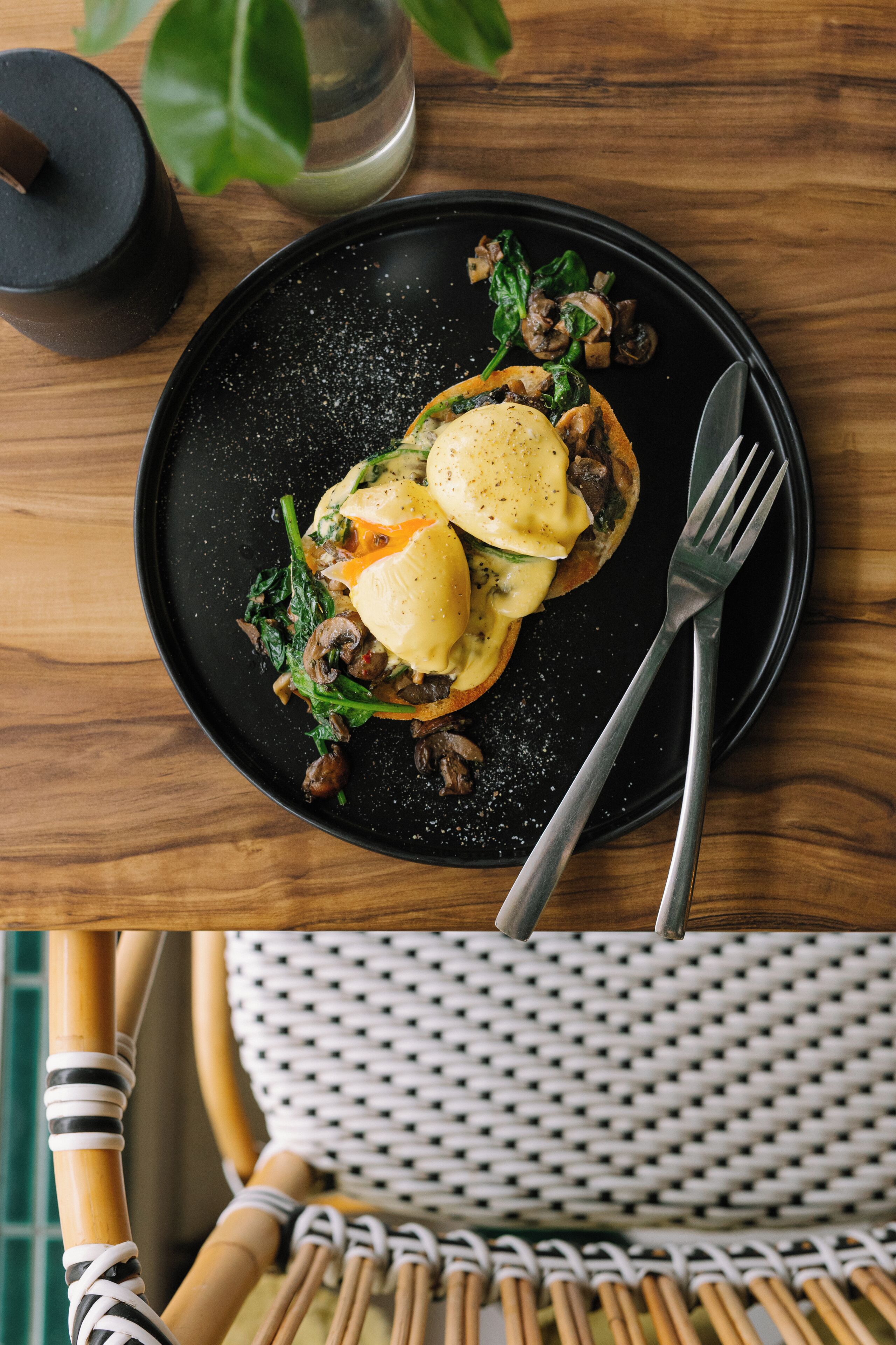 A black plate with a meal, a fork, and a glass of water on a wooden table.