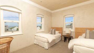 Quarto de hotel com duas camas de solteiro, uma cadeira de vime e uma mesinha de cabeceira com abajur.