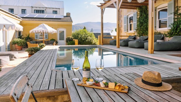 A wooden deck with a pool, outdoor seating, and a bottle of wine. - Auberge Burgundy Guest House (Hermanus)