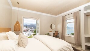 A bedroom with a large bed, a hanging light fixture, a desk with a chair, a window with curtains, and a view of the city. - Auberge Burgundy Guest House (Hermanus)