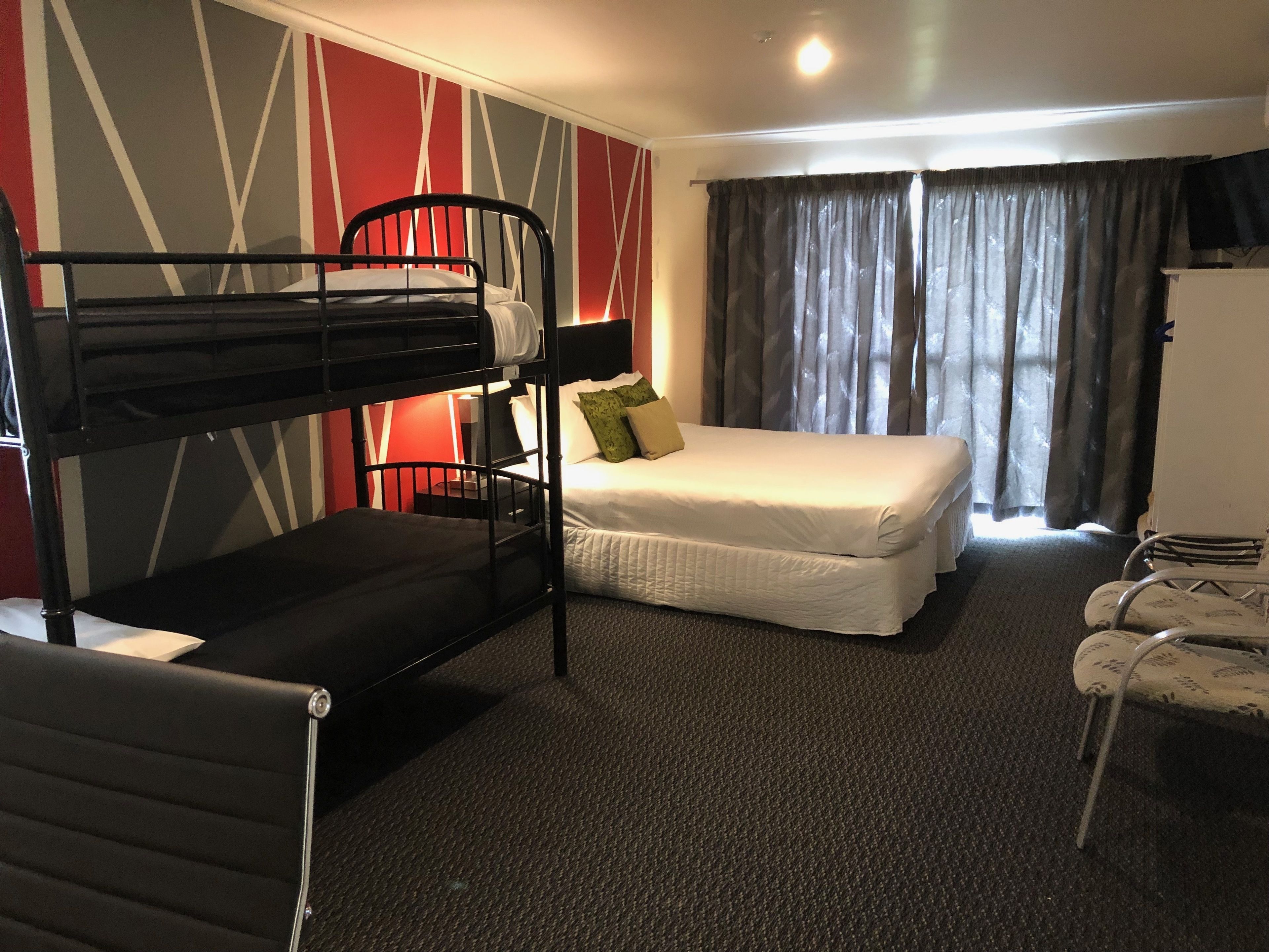 Une chambre d’hôtel avec un lit superposé, un lit simple, un bureau et une chaise.