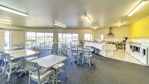 A dining area with tables and chairs, a kitchen area with appliances, and large windows offering a view. - Silver Fern Lodge (Taupo)