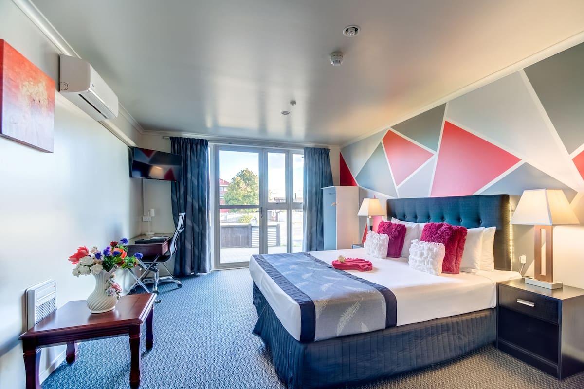 A modern hotel room with a large bed, a desk, a chair, a TV, and a view of the outdoors.