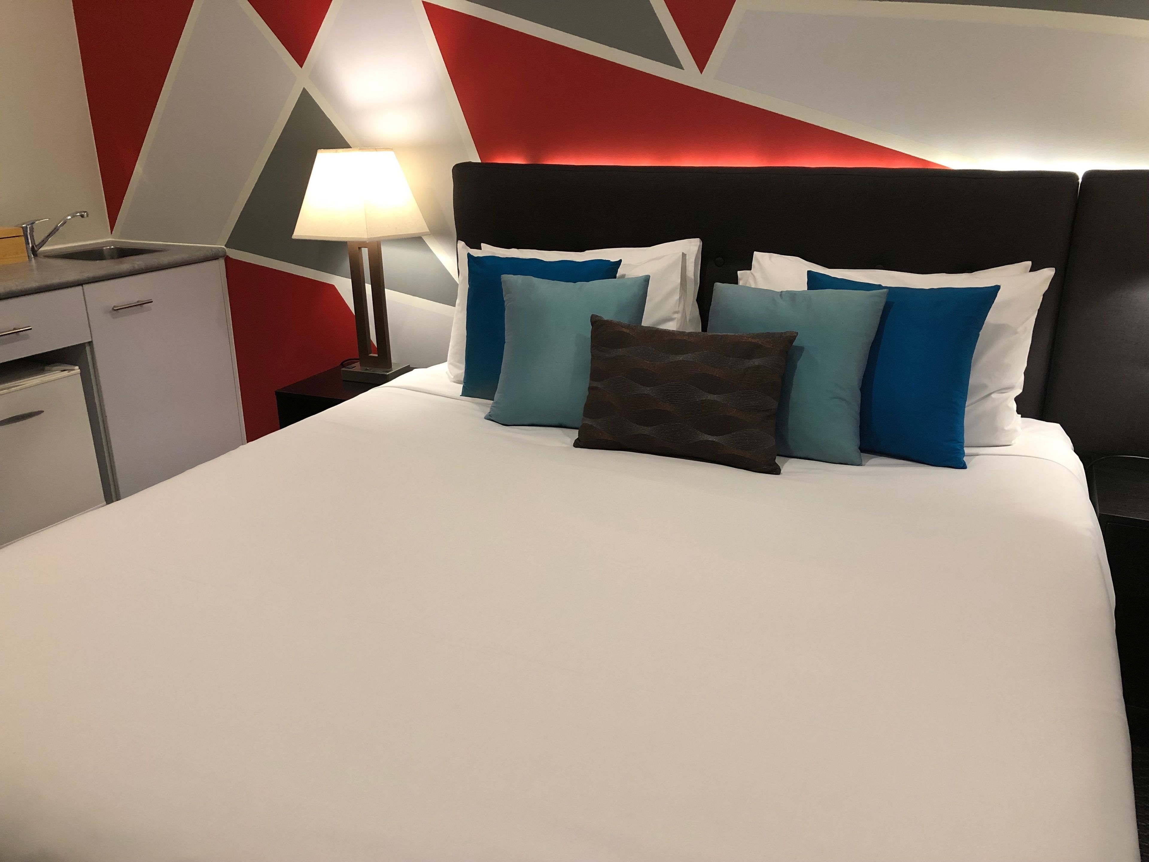 Une chambre d’hôtel avec un lit, une table de chevet, une lampe et une commode.