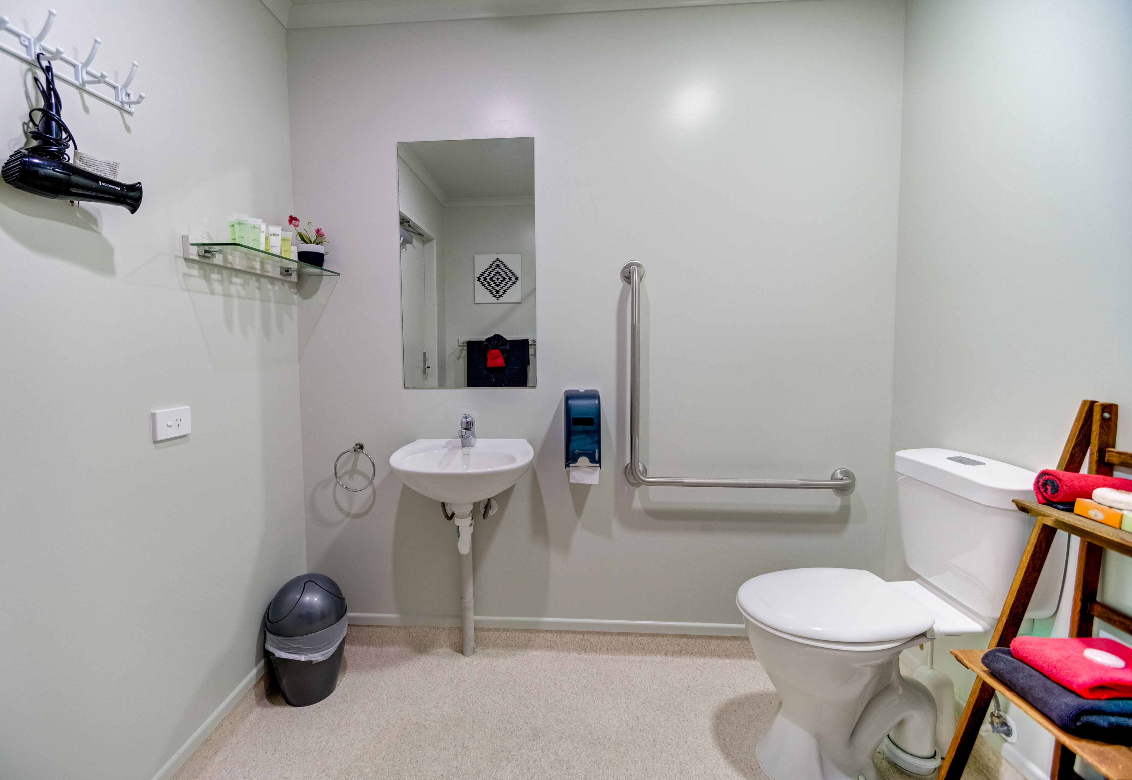 Baño pequeño con lavamanos, inodoro y pasamanos para accesibilidad.