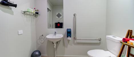 Baño pequeño con lavamanos, inodoro y pasamanos para accesibilidad.