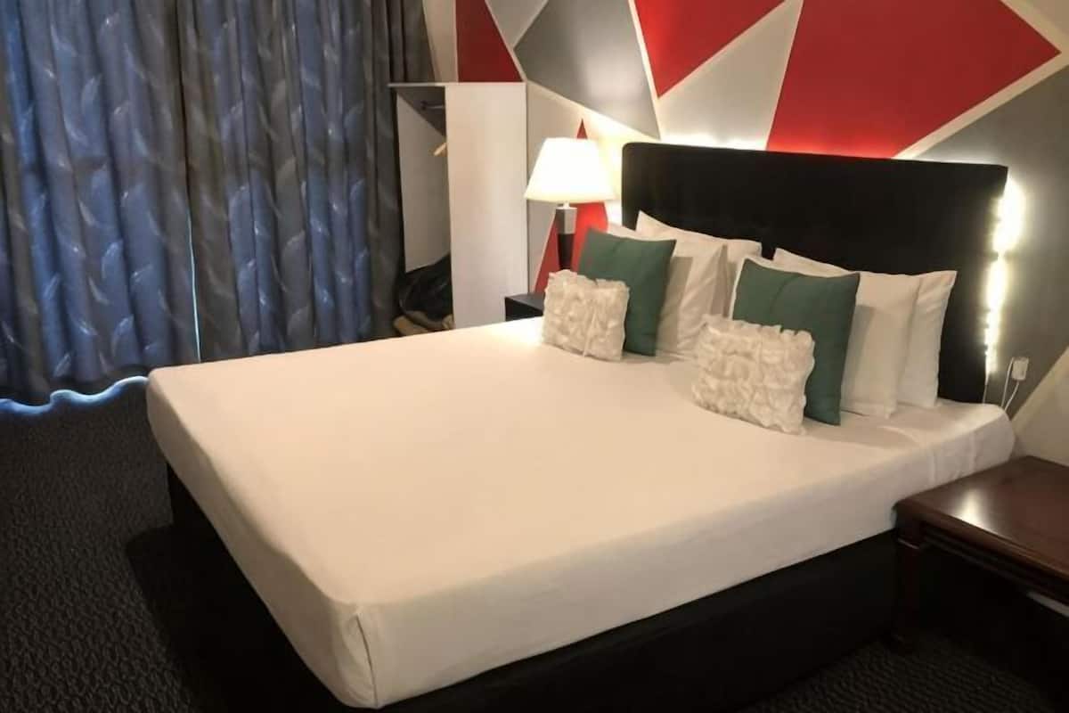 A hotel room with a large bed, a nightstand, a lamp, and a modern geometric wall design.