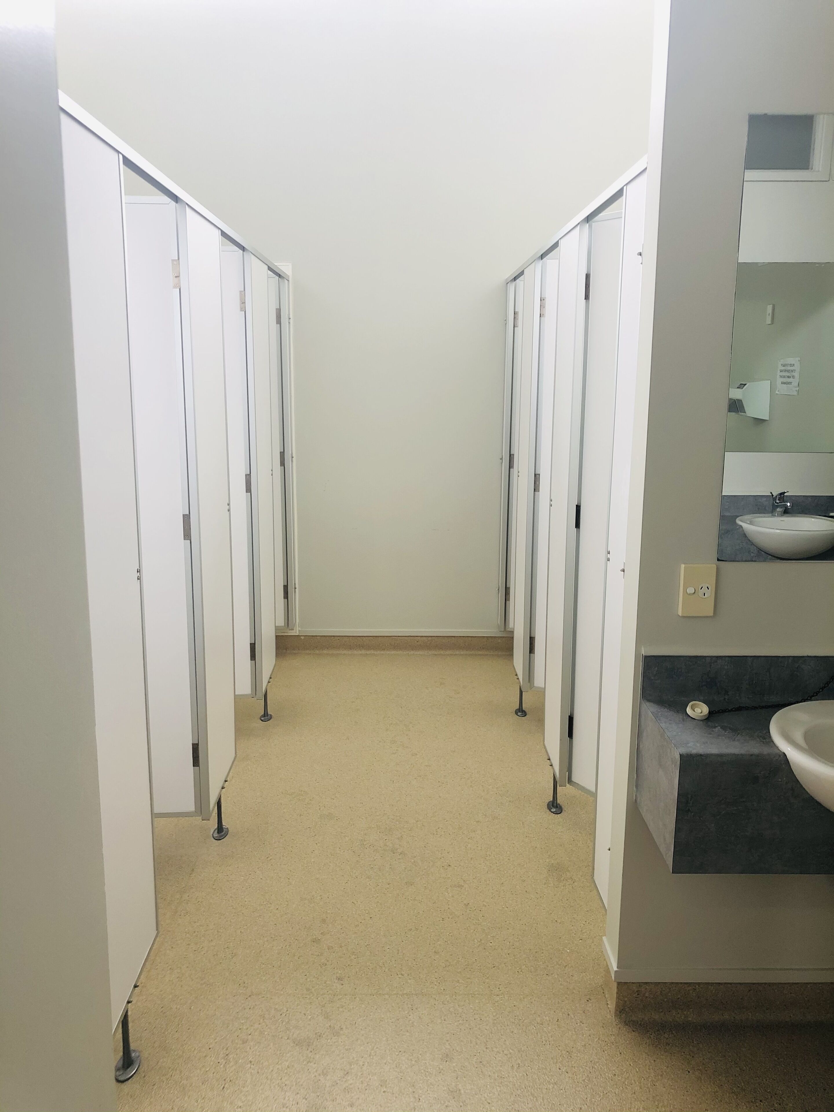 A restroom with multiple stalls, a sink, and a mirror.