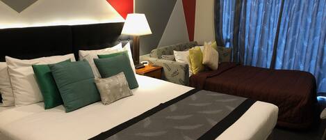 A hotel room with a large bed, a nightstand, a lamp, a sofa, and a view of the outside through curtains.