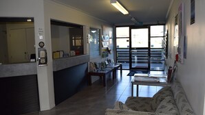 A hotel lobby with a reception desk, a sofa, a bench, and a view of the outside. - Silver Fern Lodge (Taupo)