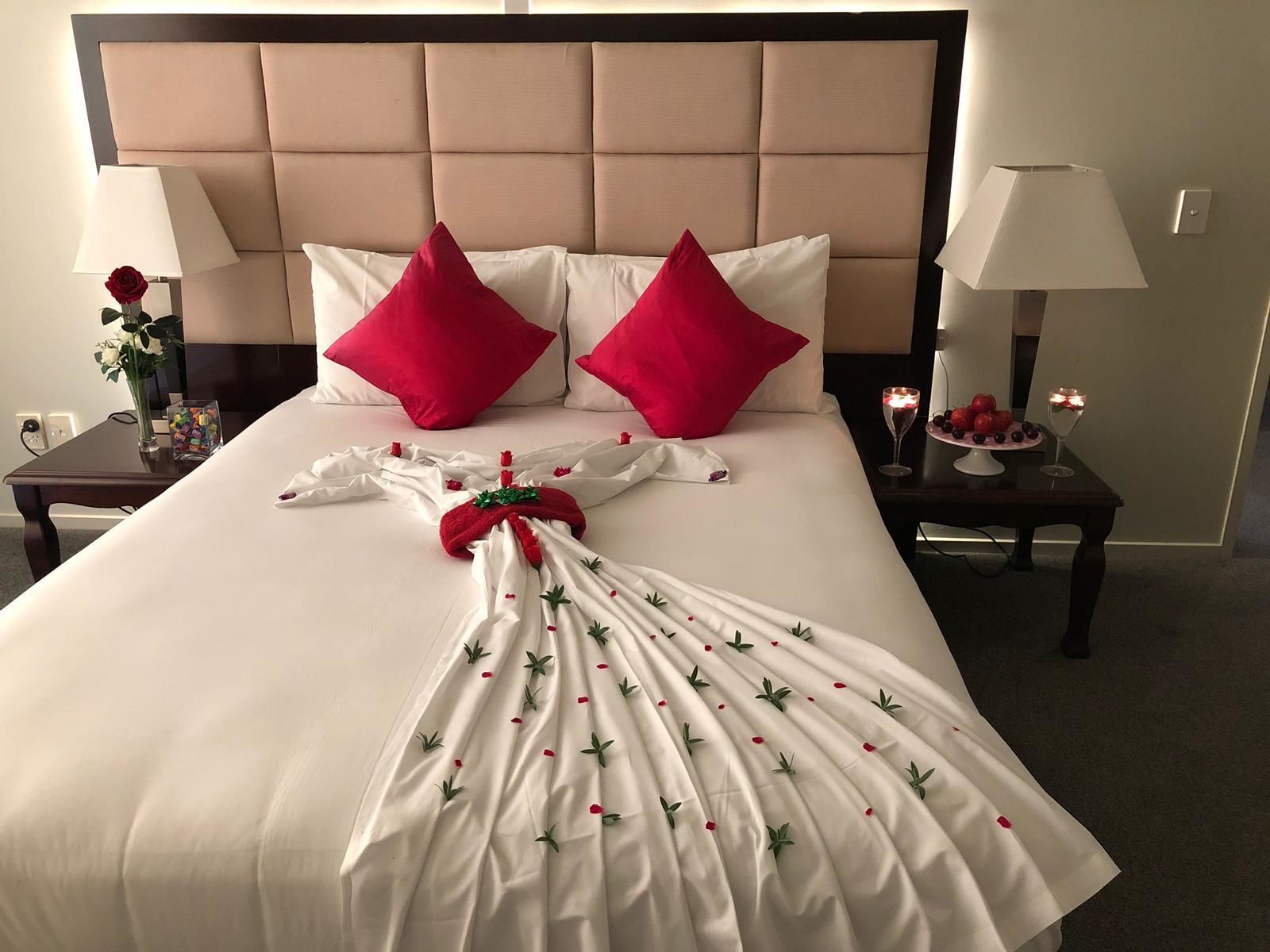 A neatly made bed with a white duvet, two red pillows, and a decorative towel with green leaves and red flowers.
