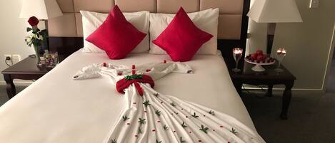A neatly made bed with a white duvet, two red pillows, and a decorative towel with green leaves and red flowers.