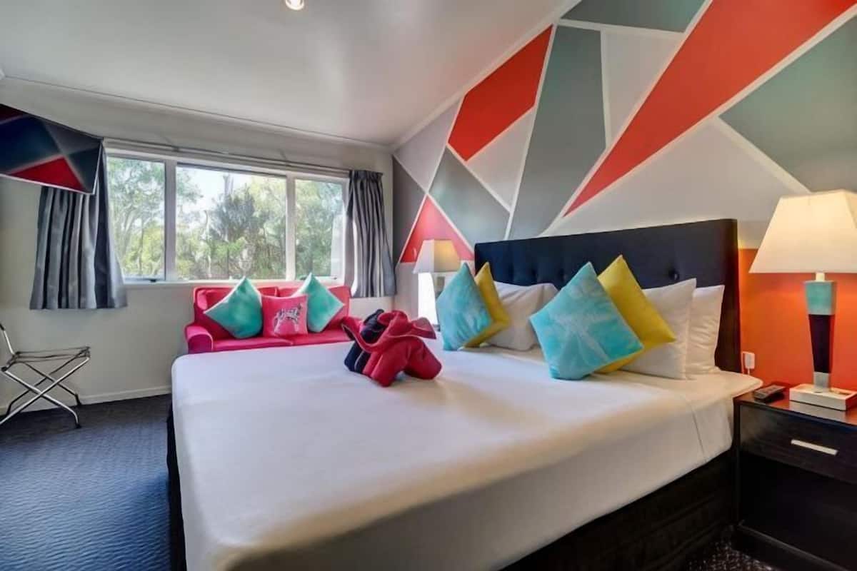 A hotel room with a large bed, a desk, a chair, and a window with curtains.