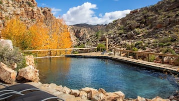 Zona de piscina con terraza de madera, sillas de descanso y paisaje rocoso al fondo.