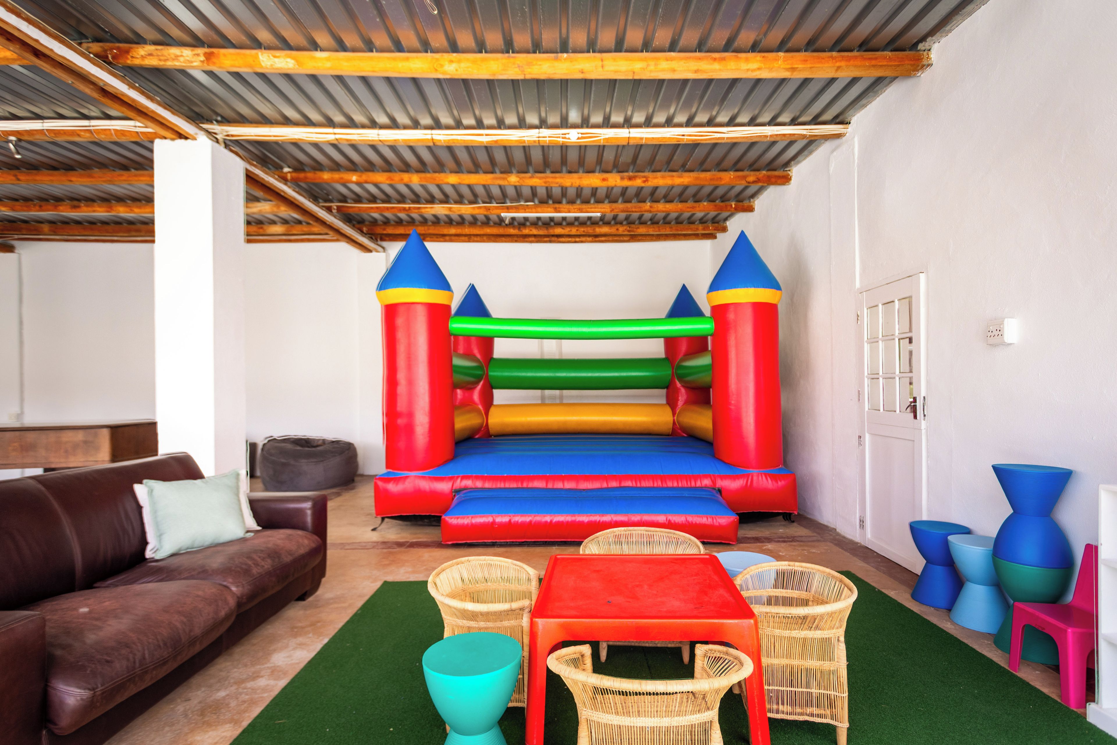 Une pièce avec un trampoline, un canapé marron, des fauteuils en osier et une petite table.