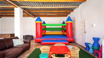 Une pièce avec un trampoline, un canapé marron, des fauteuils en osier et une petite table.