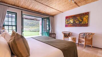 A bedroom with a bed, two chairs, a painting, and a view of the outdoors.