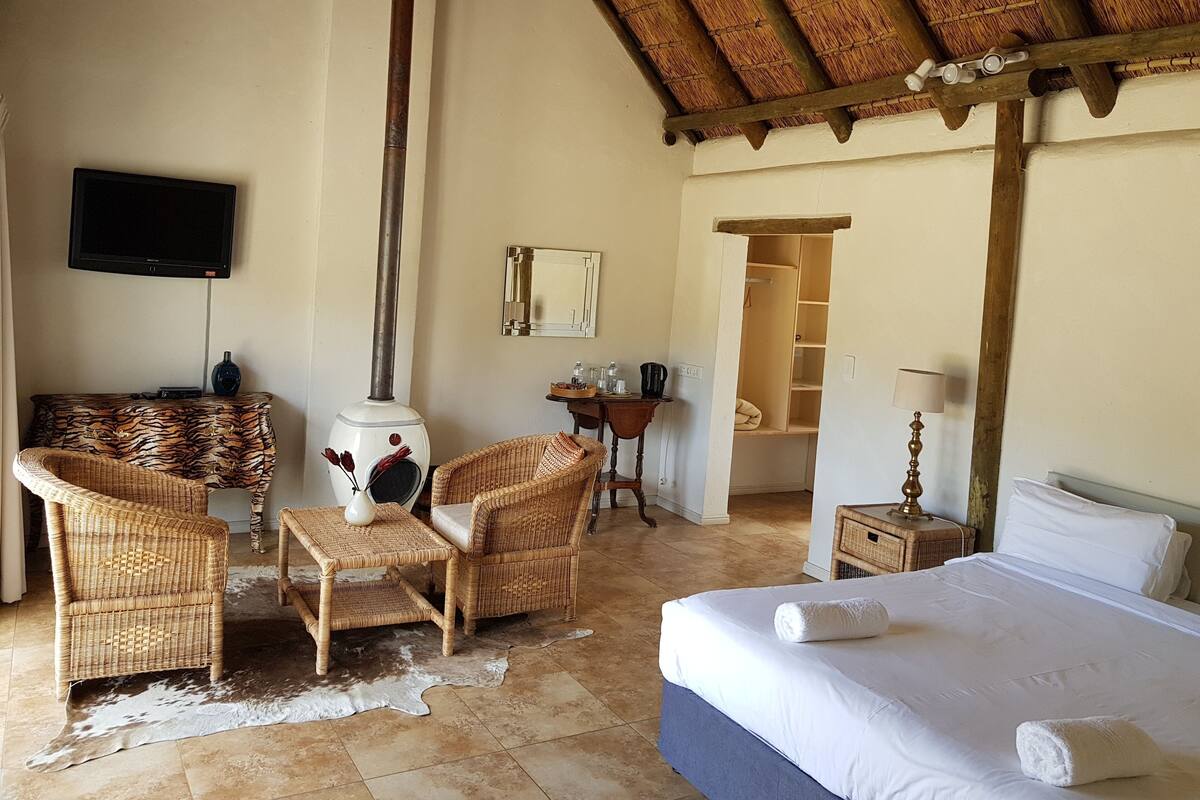 Hotelkamer met een bed, twee rieten stoelen, een tafeltje, een televisie, een open haard, een kledingkast en een lamp.