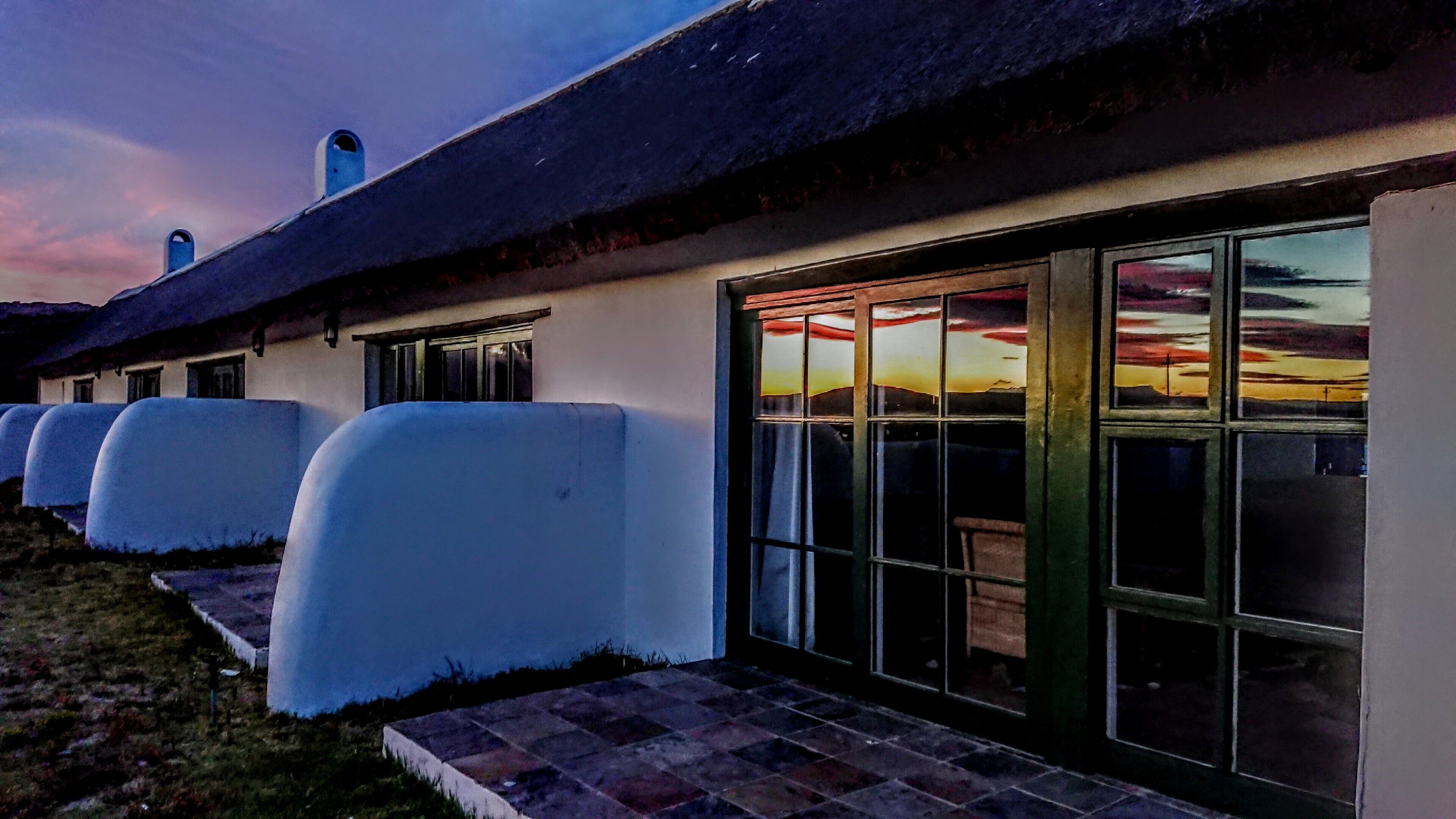 Une rangée de bâtiments blancs, avec des toits de chaume, de grandes fenêtres et une vue sur le coucher de soleil.