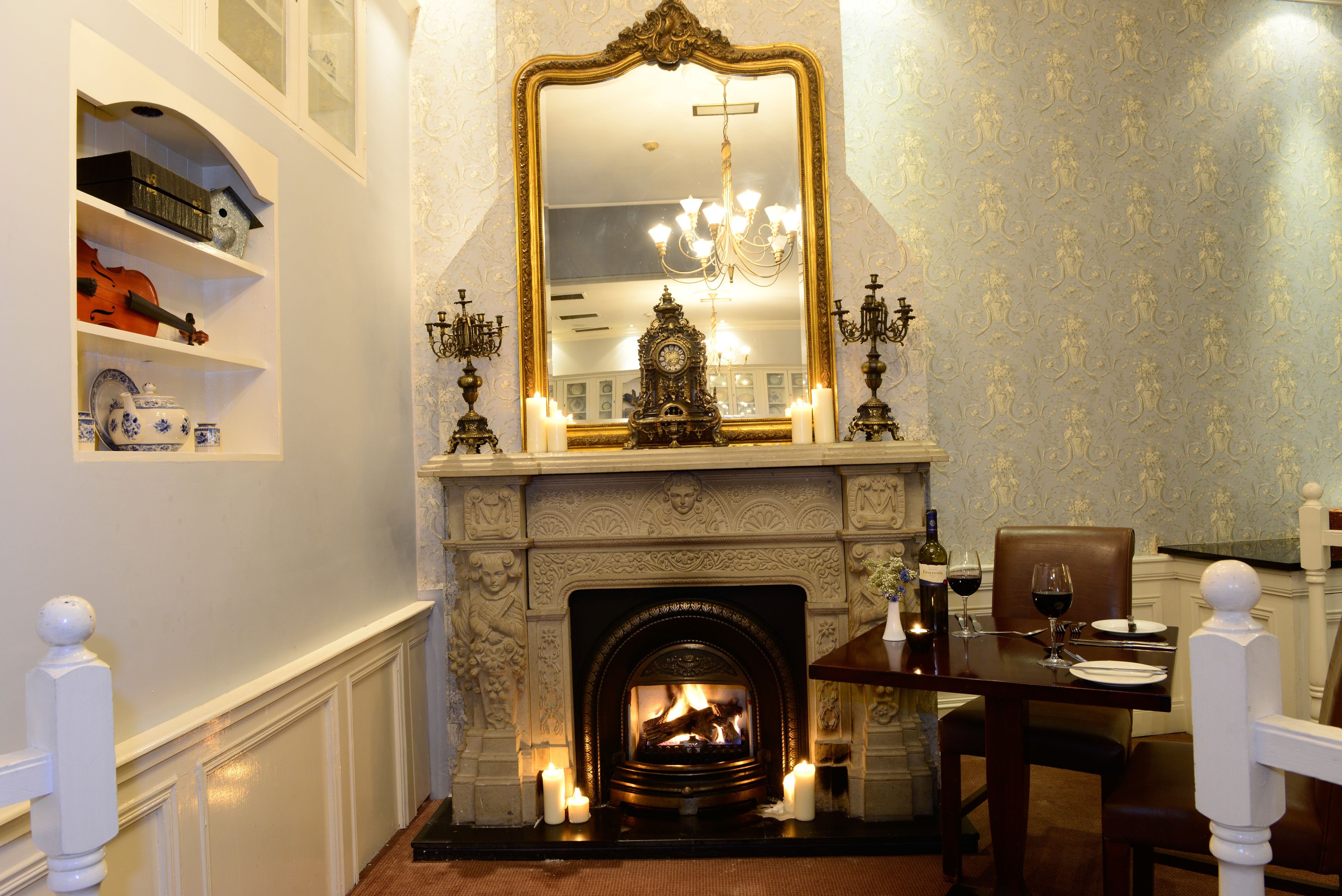 A dining area with a fireplace, candles, and a chandelier.