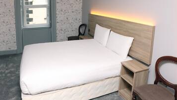 Ein ordentlich bezogenes Bett mit Holz Kopfteil, ein Nachttisch und ein Stuhl in einem Zimmer mit Ziegelmuster Wand und einem Fenster.