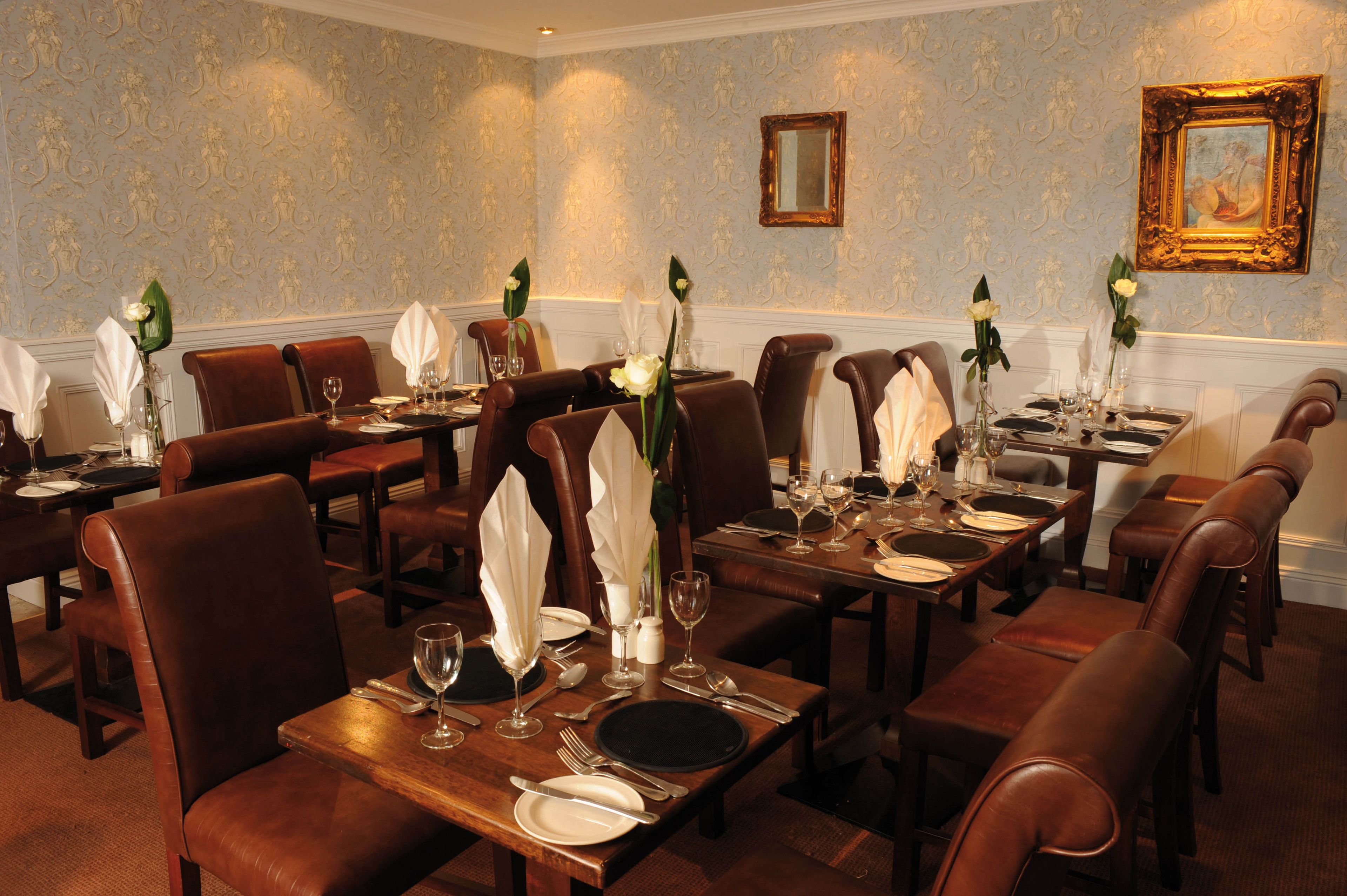 Comedor formal con varias mesas dispuestas para el servicio, sillas elegantes y diseños decorativos en las paredes.