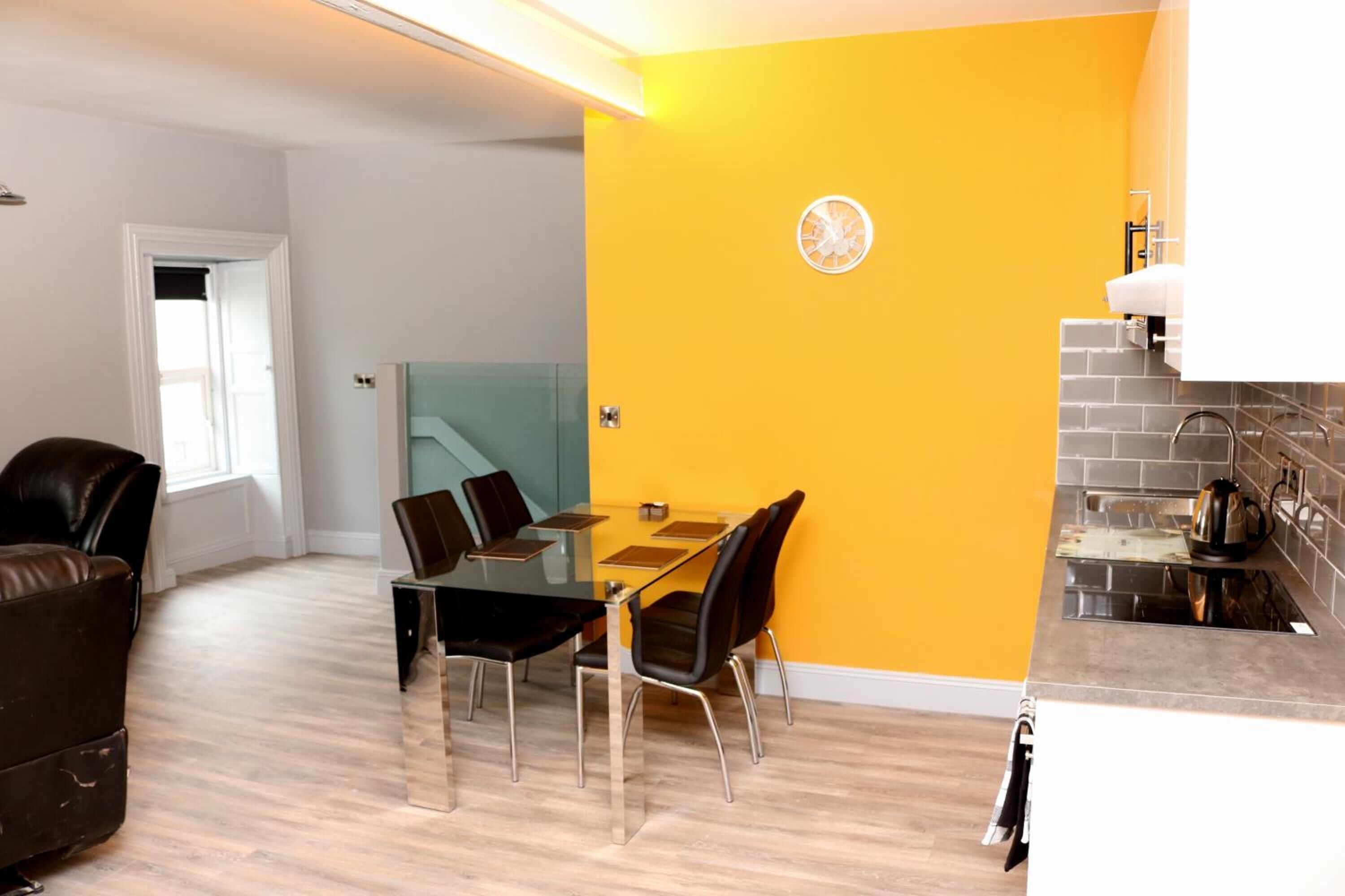 Un espace de vie moderne comprenant un coin repas, une cuisine et un mur d’accent d’un jaune vif.