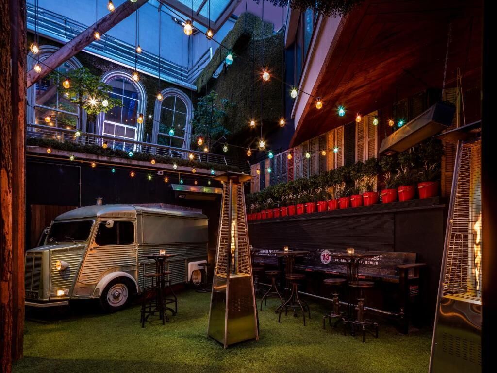A rooftop bar with a vintage truck, outdoor seating, and string lights.