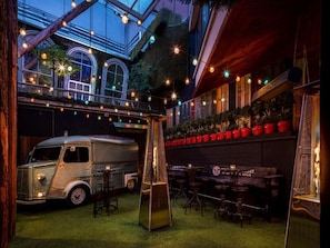 Un bar en la azotea con un camión antiguo, mesas al aire libre y guirnaldas de luces.