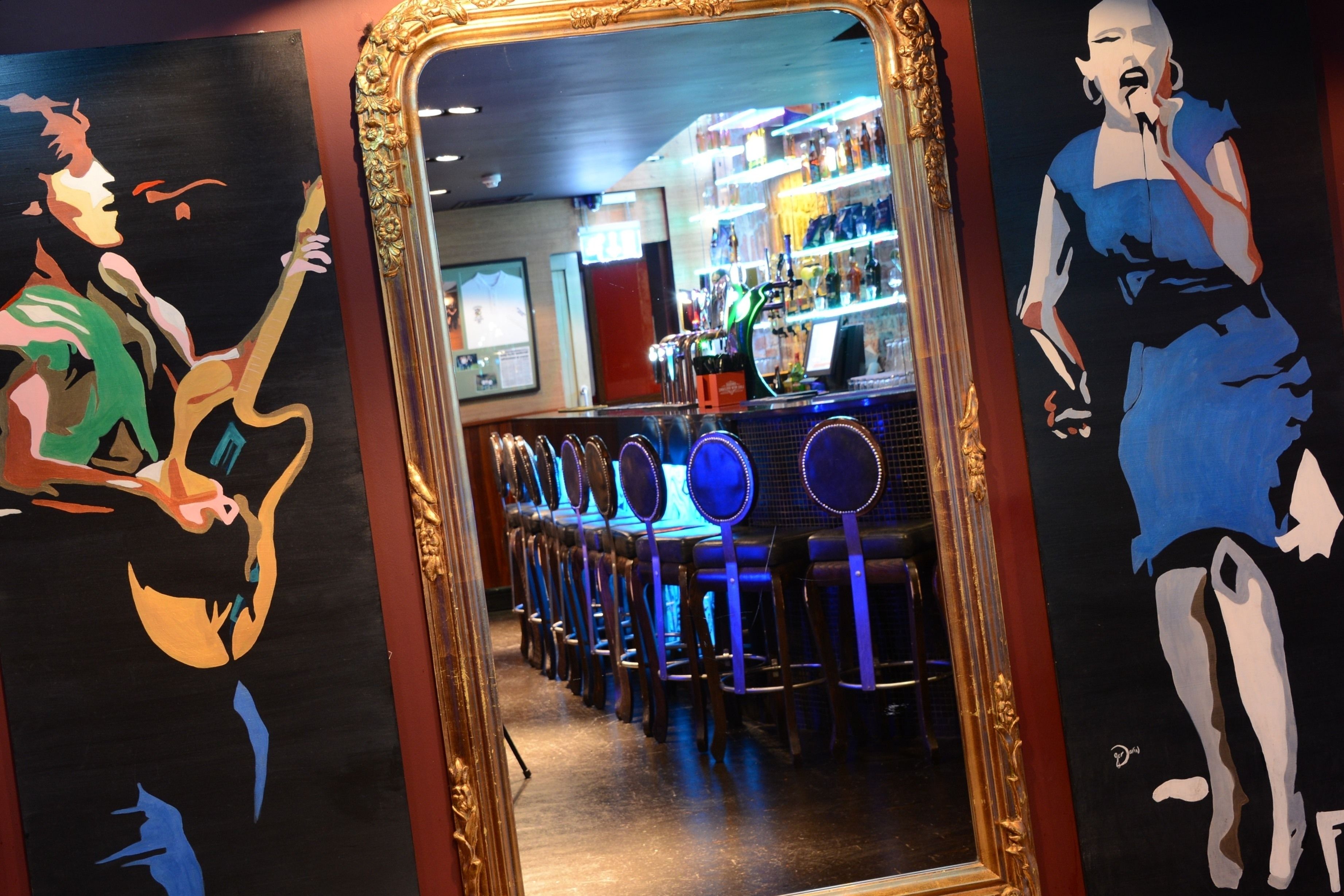 A bar area with a long counter, multiple bar stools, and a mirror reflecting the interior.