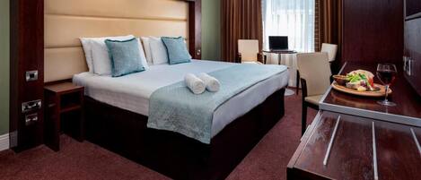 Una habitación de hotel con una cama grande, un escritorio con una silla, un televisor y un área de comedor con un plato de comida y una copa de vino.