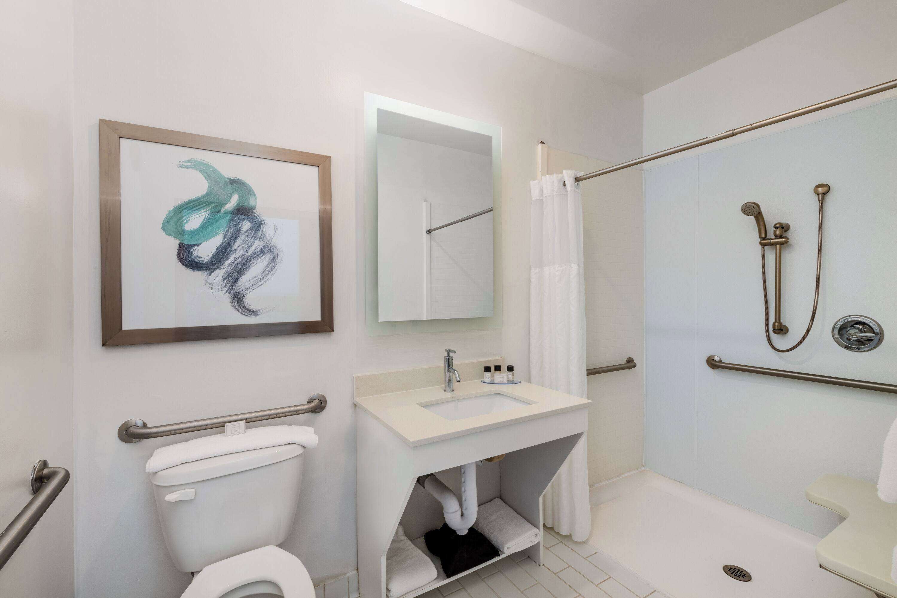 A modern bathroom with a toilet, sink, shower, and a framed abstract painting.