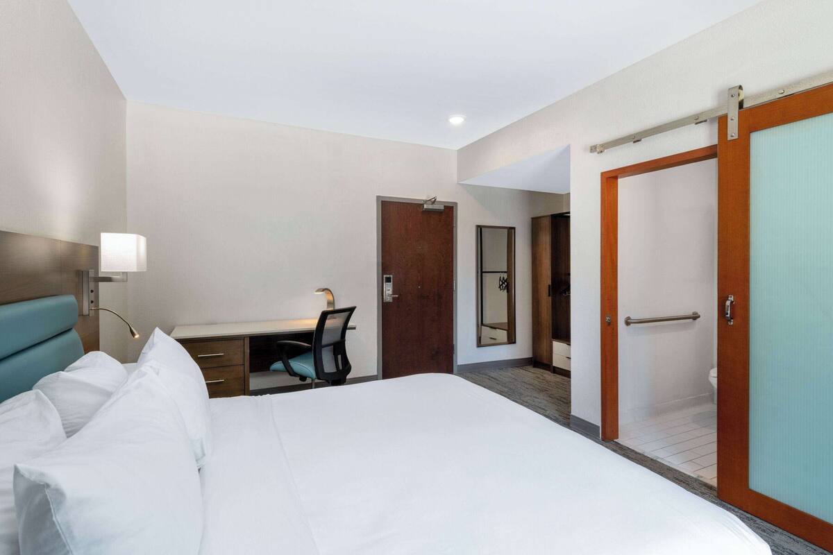 Une chambre d’hôtel comprenant un lit, un bureau, une chaise et une salle de bain avec douche et toilettes.