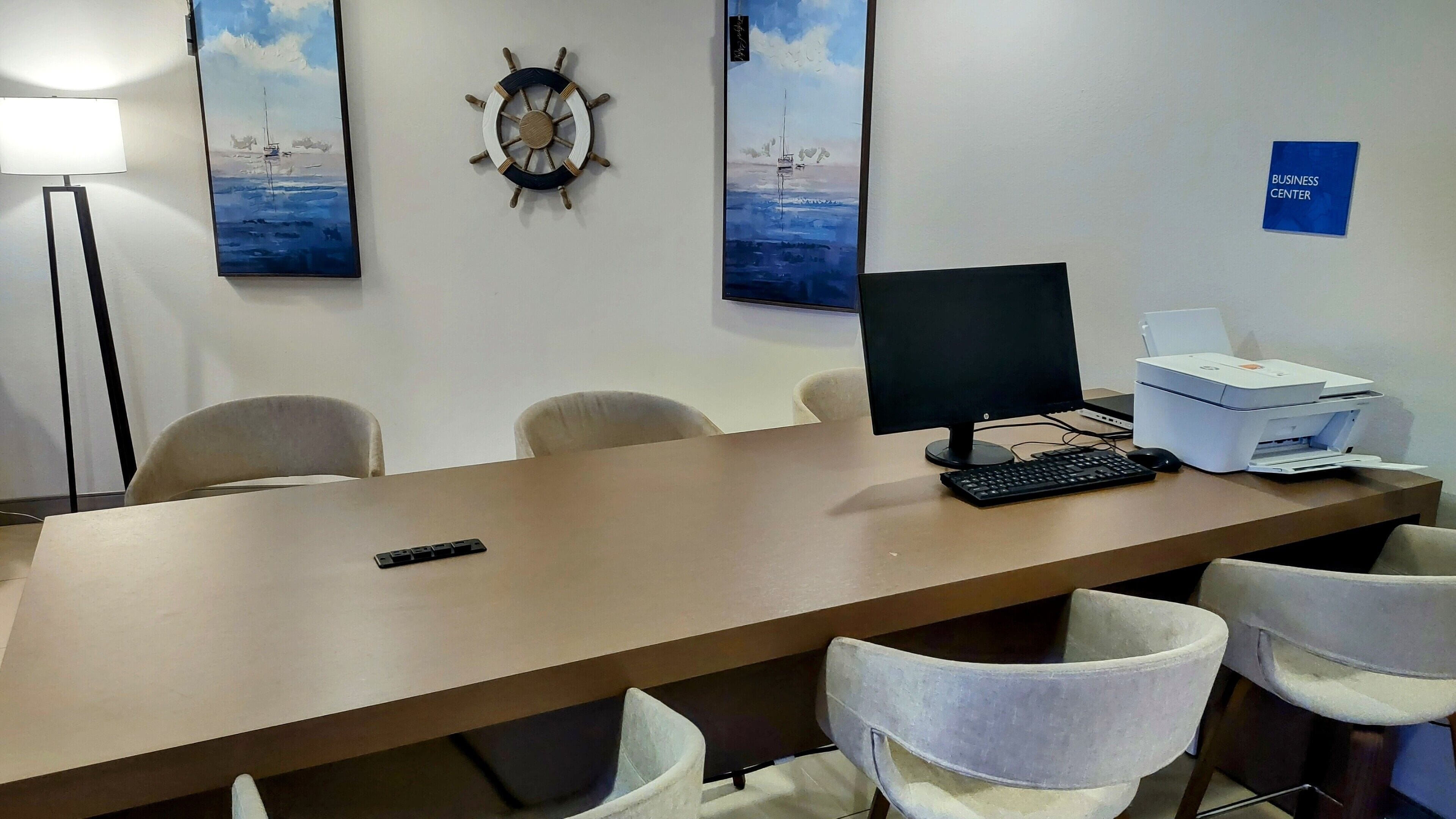 Ein Konferenzraum mit einem langen Tisch, vier Stühlen, einem Desktop-Computer, einem Drucker und zwei Bildern an der Wand.
