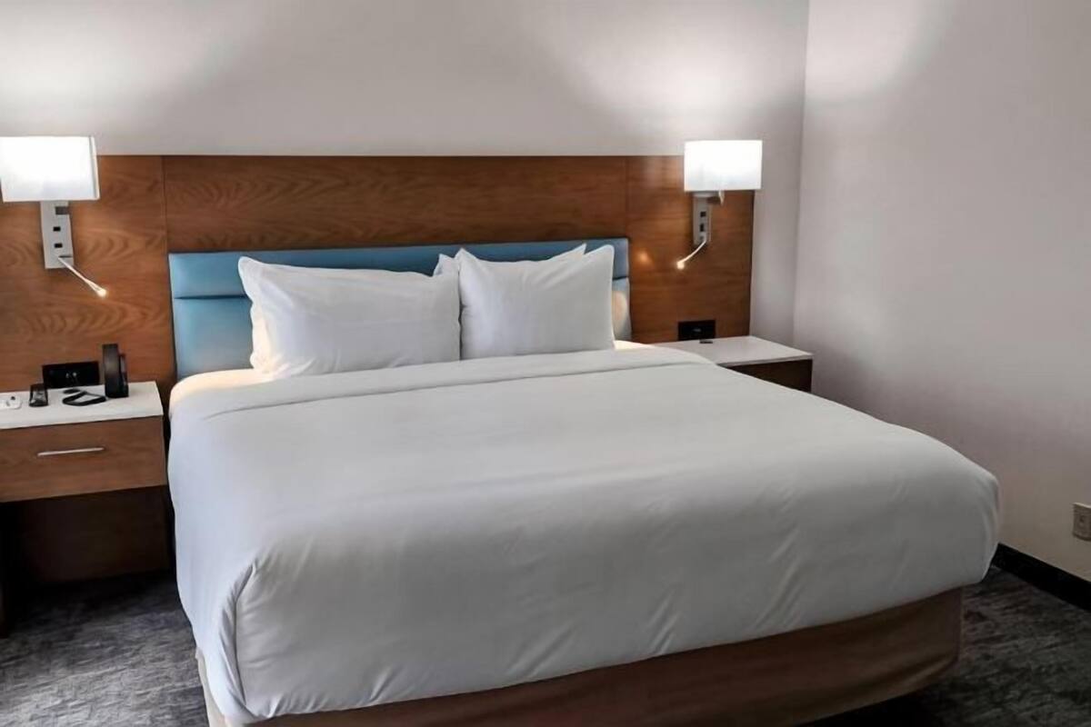 Une chambre d’hôtel avec un grand lit, une tête de lit en bois, deux tables de chevet et des lampes fixées au mur.