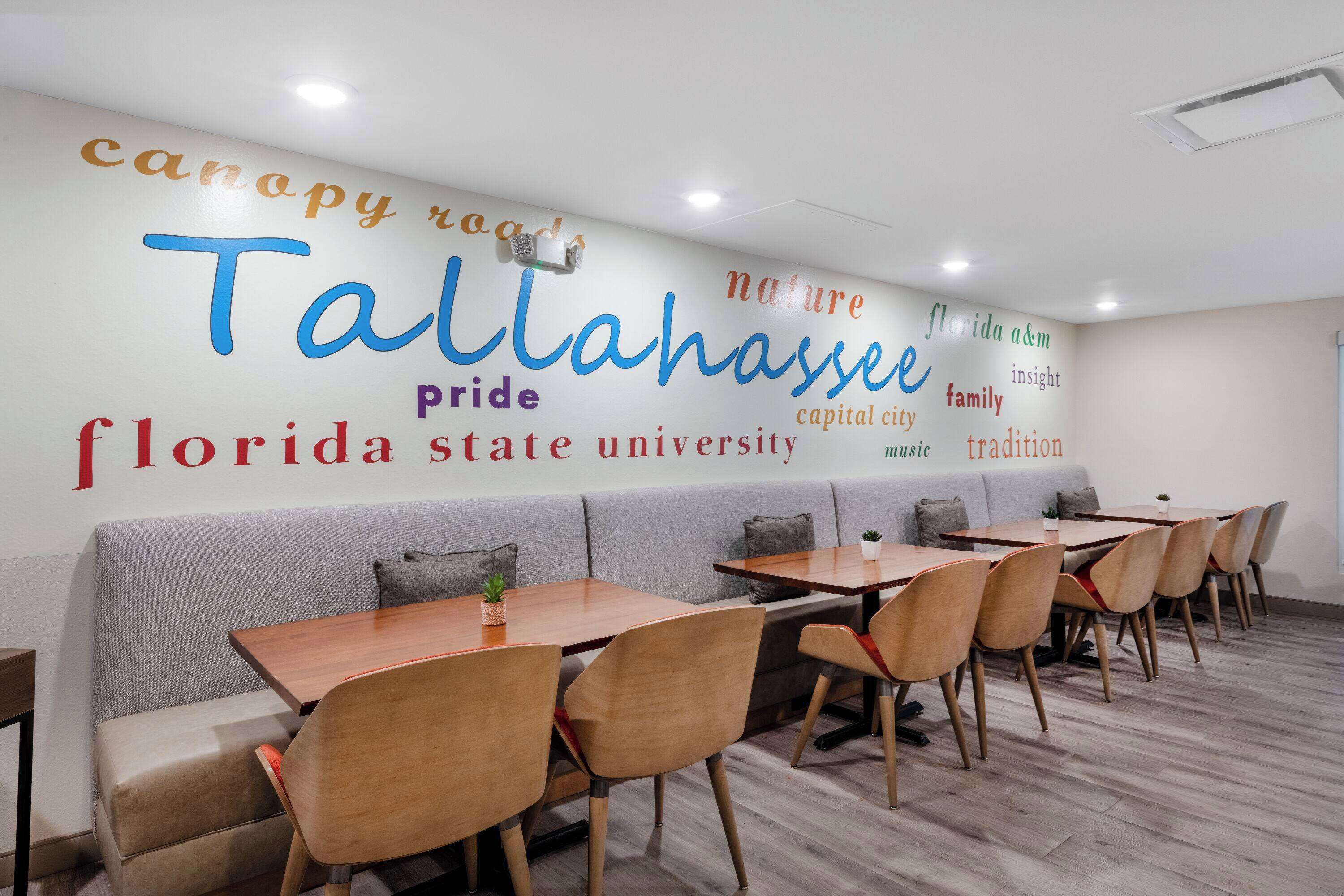 A dining area with tables and chairs, a sofa, and a wall with words like "Florida State University" and "Tallahassee".