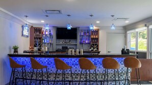 A bar area with a tiled backsplash, bar stools, shelves with bottles, and a flat-screen TV.