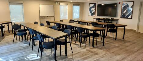 A conference room with multiple tables and chairs, a whiteboard, and a large flat-screen TV on the wall.