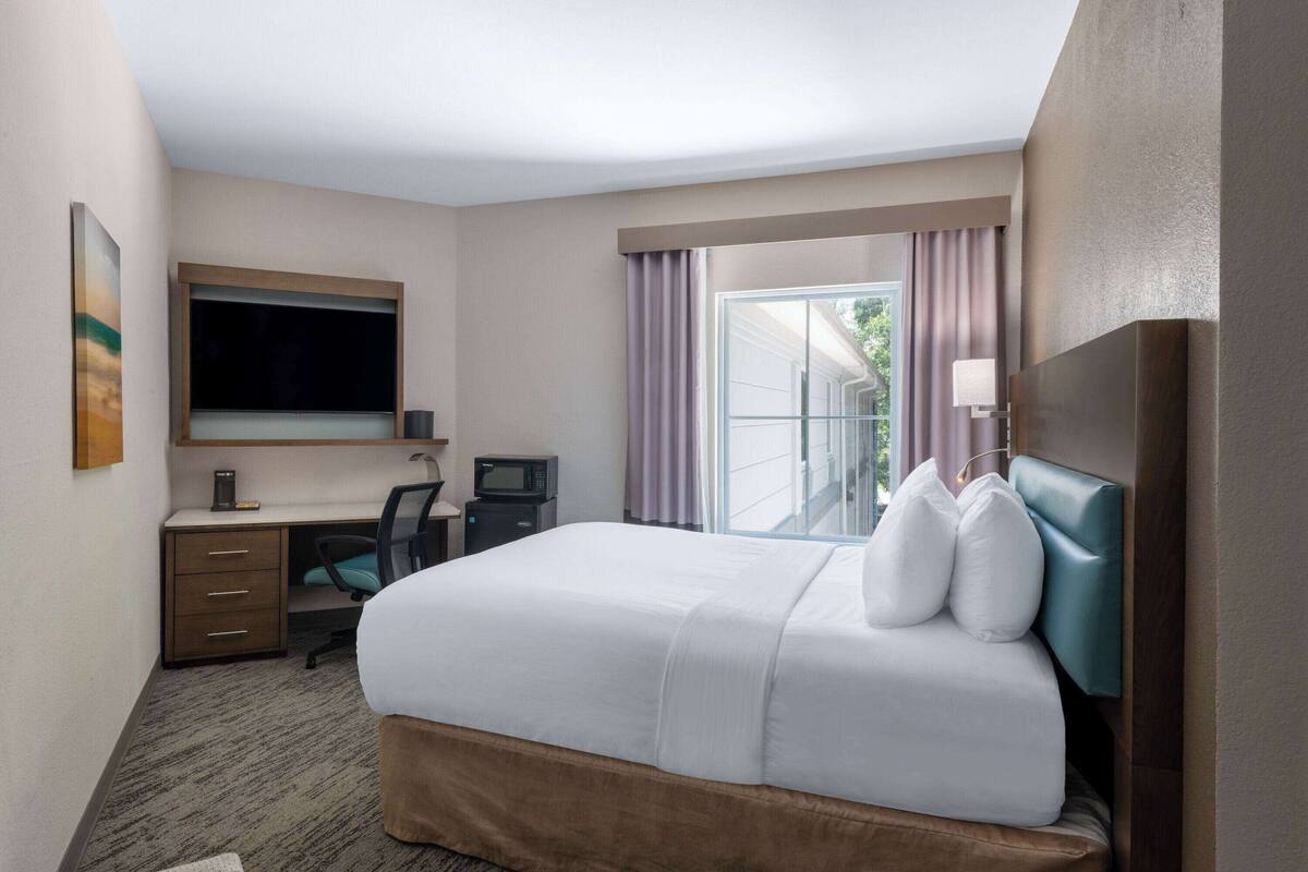 Une chambre d’hôtel avec un grand lit, un bureau avec un ordinateur, une télévision et une vue sur l’extérieur.