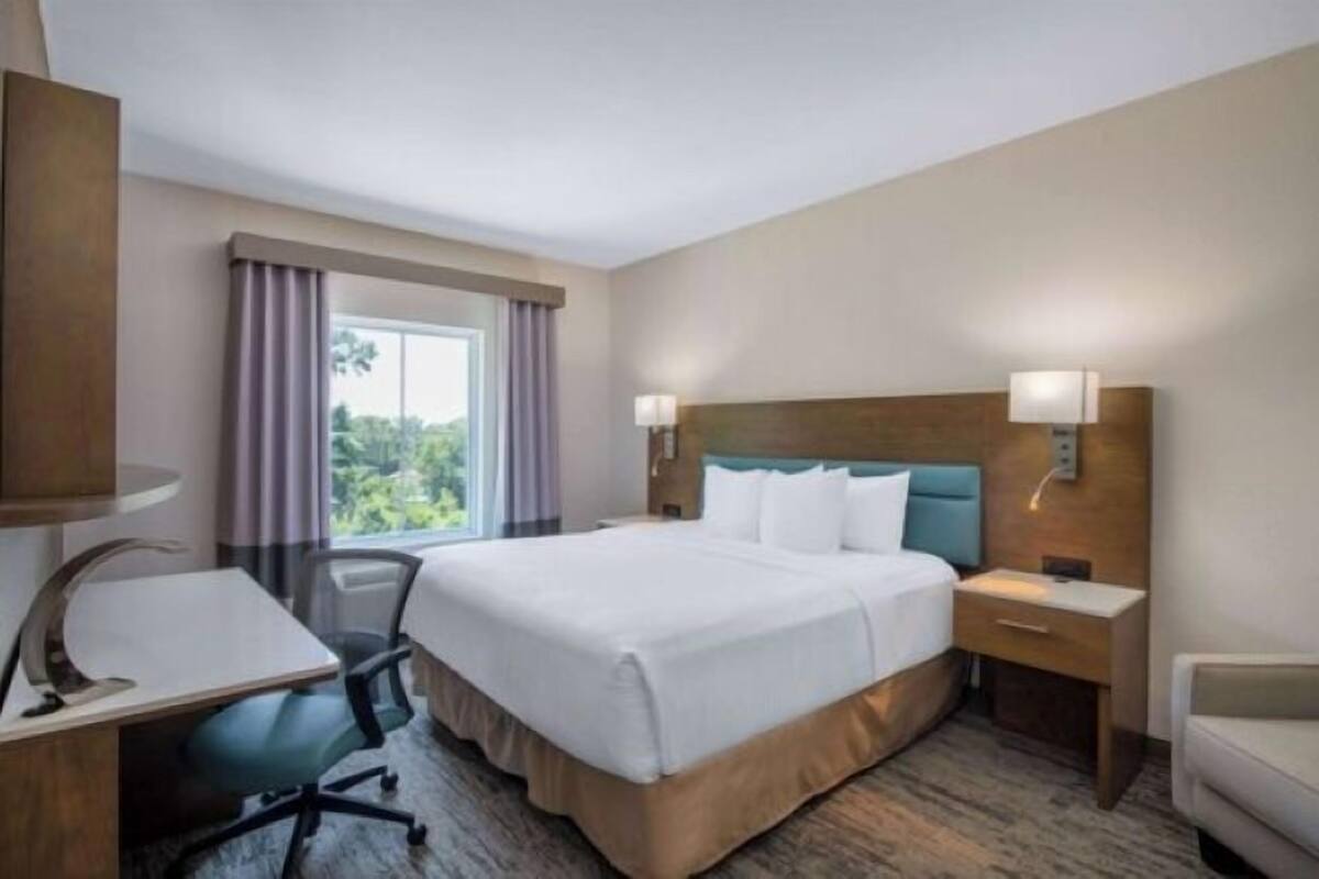 Une chambre d’hôtel avec un grand lit, un bureau, une chaise, une table de chevet et une fenêtre avec des rideaux.