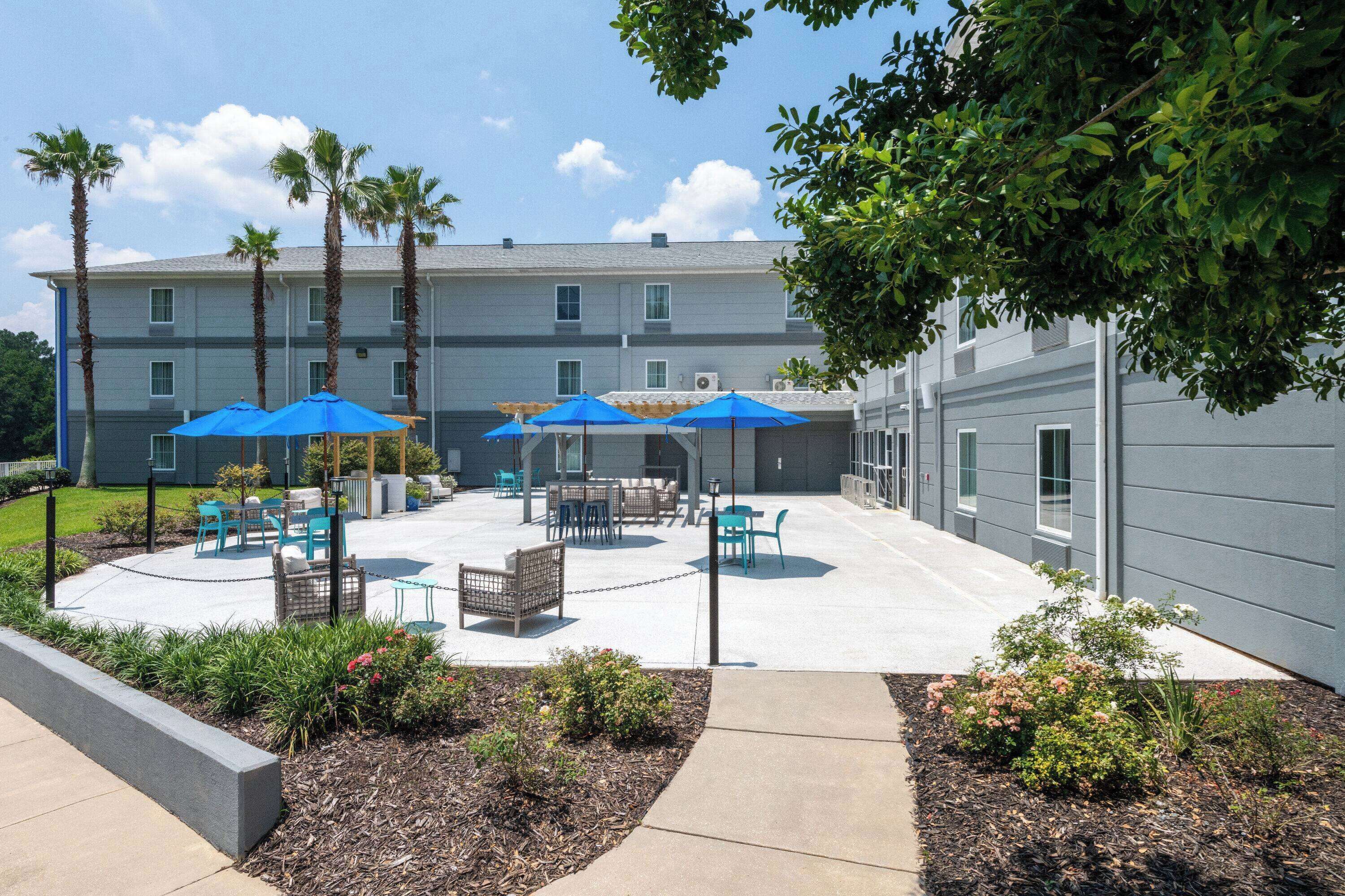 A courtyard with outdoor seating, palm trees, and a building with multiple windows.