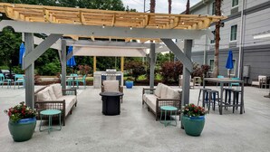 An outdoor patio area with a pergola, seating arrangements, and a barbecue grill.
