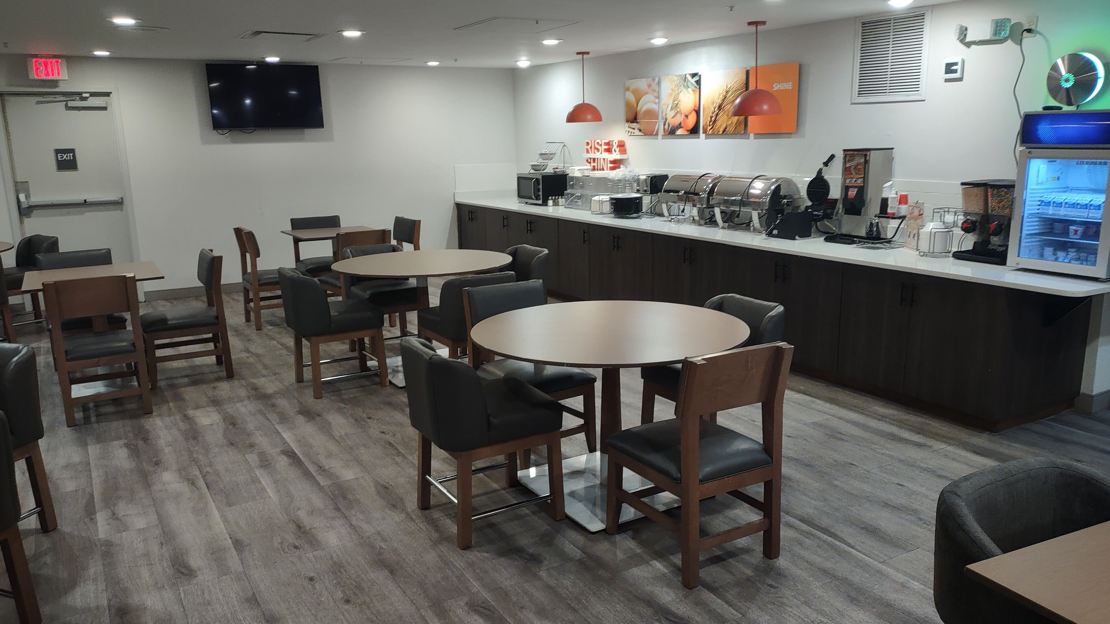 Un restaurant moderne avec des tables et des chaises rondes, un comptoir avec une machine à café et un téléviseur fixé au mur.