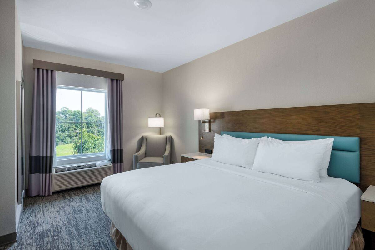Une chambre d’hôtel avec un grand lit, une chaise, une table de chevet et une fenêtre avec des rideaux.